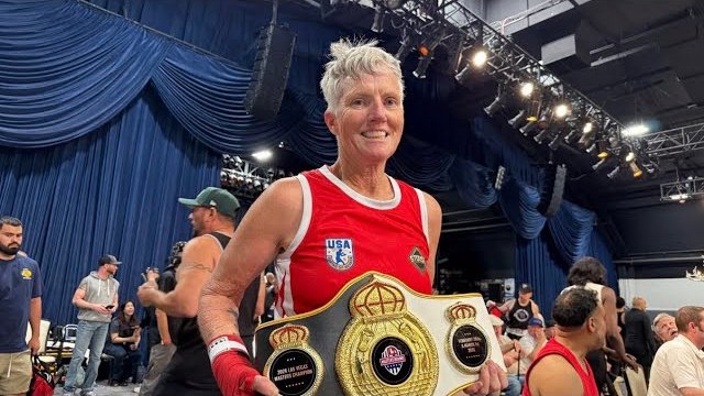 Cindi West smiling with her championship belts at a boxing event